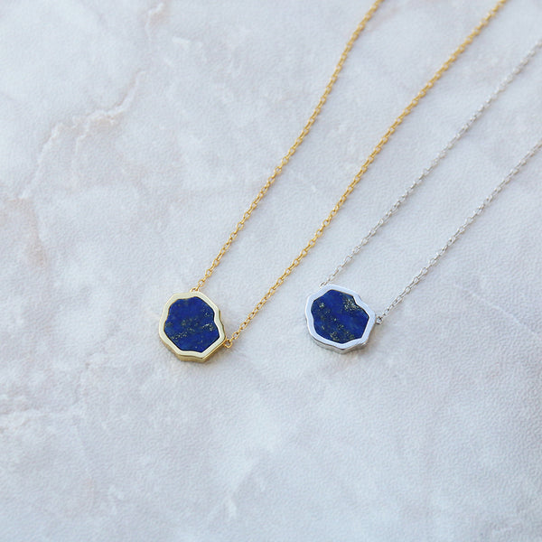 Two bright blue lapis lazuli with gold flecks necklaces on marble background in sterling silver and 14k gold