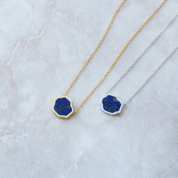 Two bright blue lapis lazuli with gold flecks necklaces on marble background in sterling silver and 14k gold